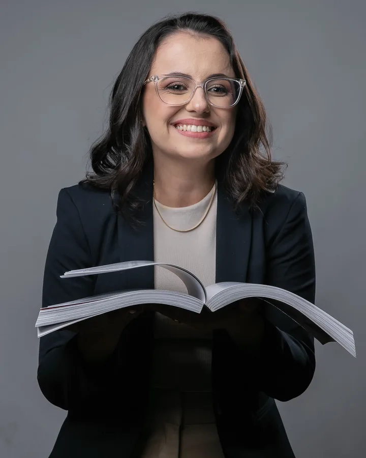 Profa. Ana Ester sorrindo, com um livro aberto nas mãos